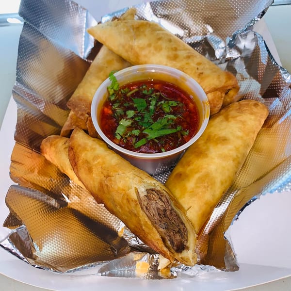Crispy Chido's Tacos flautas with a side of red salsa topped with cilantro, served in foil.