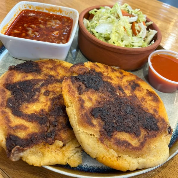 Two golden-brown Chido's Tacos pupusas with charred spots, served with red sauce and cabbage salad.