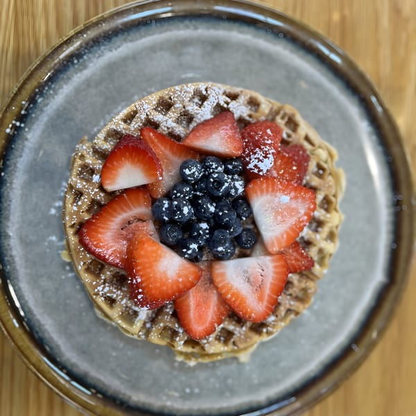 Waffle topped with fresh strawberries, blueberries, and powdered sugar on a gray plate.