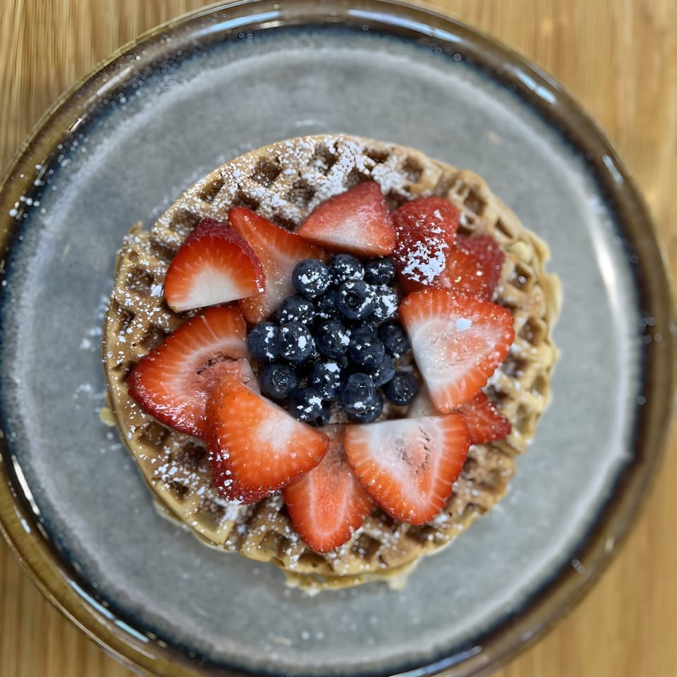 Waffle topped with fresh strawberries, blueberries, and powdered sugar on a gray plate.