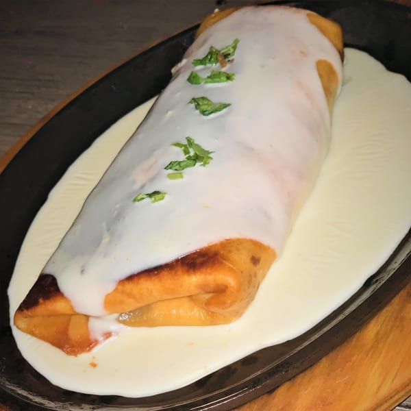 Chido's Tacos' golden-brown chimichanga, generously covered in creamy white sauce and fresh green herbs.