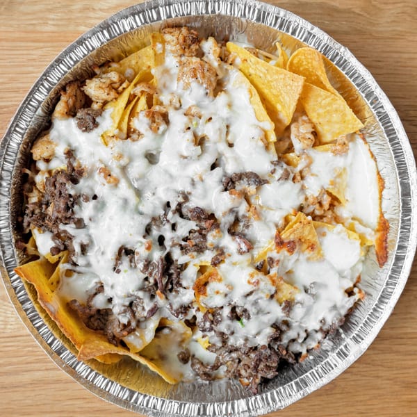 Chido's Tacos nachos with melted white cheese, ground beef, and chicken in a foil container.
